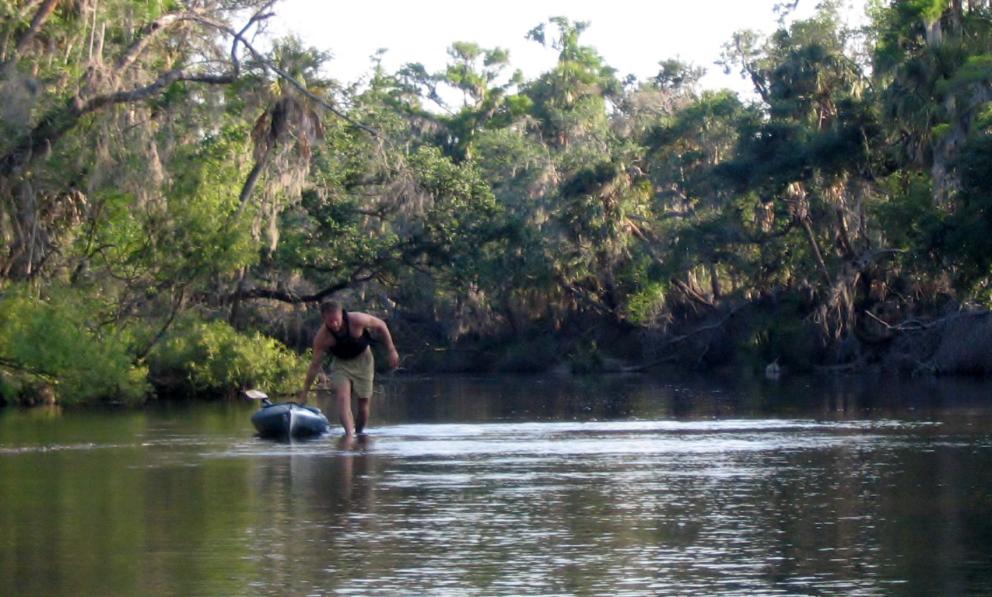 A kayaker drags his boat through shallow water