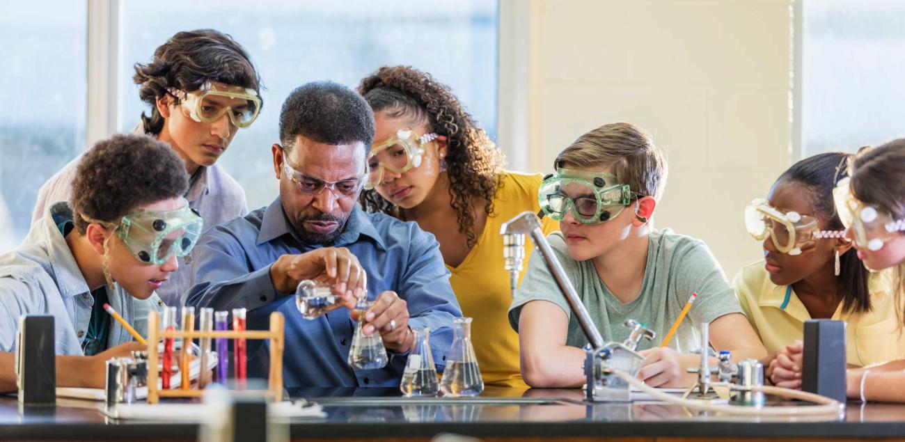 Teacher conducting an experiment in science lab surrounded by students