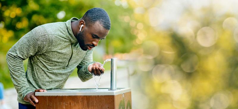 athletic man drinking from outdoor water fountain